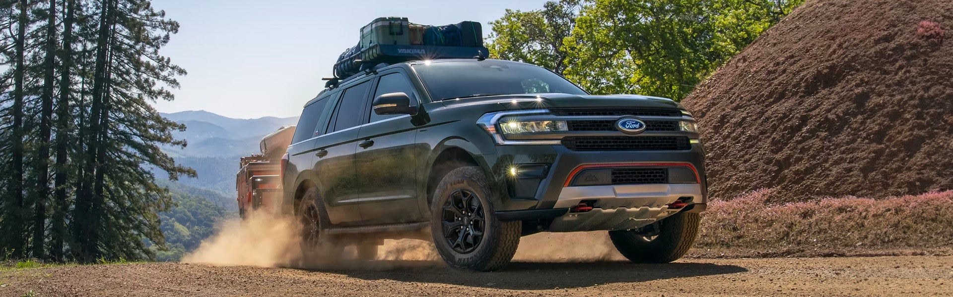 Un todoterreno Ford SUV remolcando un remolque por un camino de tierra en un entorno montañoso.