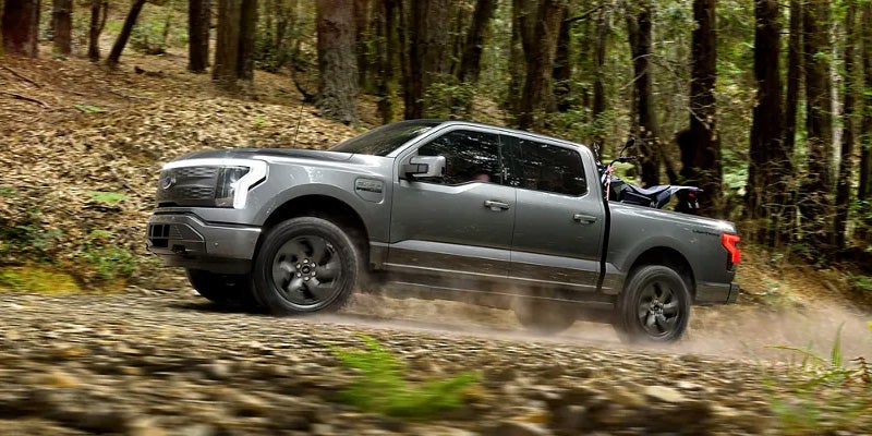 electric pickup truck driving on a dirt forest path