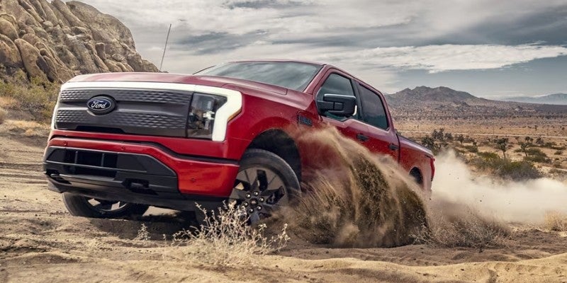 Una camioneta pickup Ford F-150 Lightning circulando por el desierto con arena proyectándose desde las ruedas delanteras.