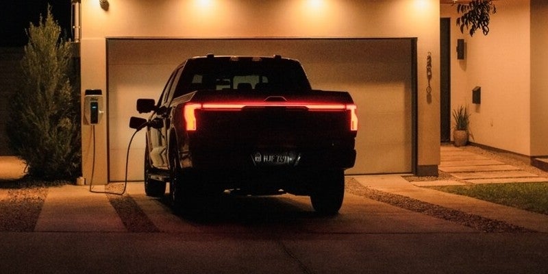 Una camioneta pickup Ford F-150 Lightning estacionada en el garaje de una casa y conectada a un cargador doméstico.