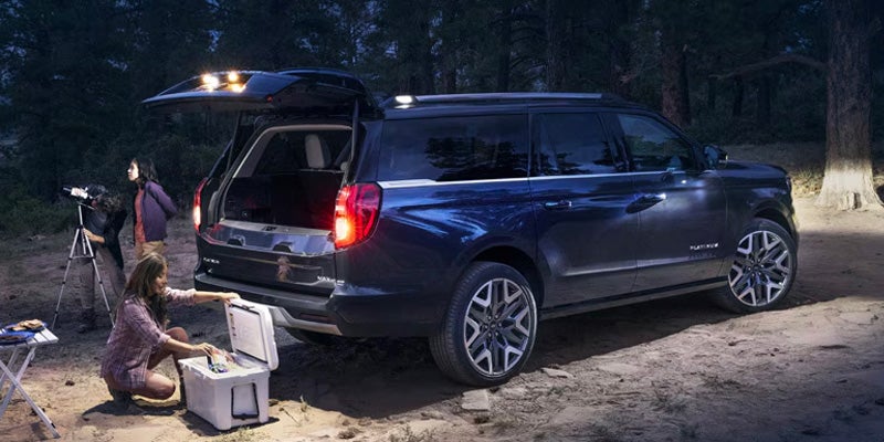 Puerta trasera de una Ford Expedition abierta, con equipaje en el maletero y una chica sentada detrás del coche.