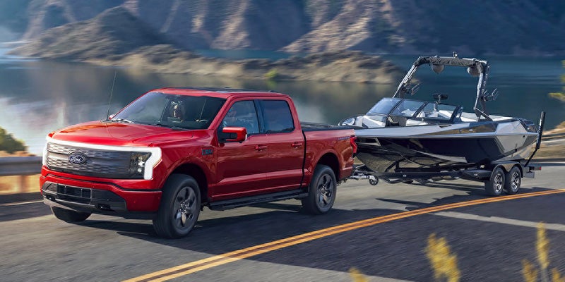 Una camioneta pickup F-150 Lightning de Ford circulando por una autopista con un remolque de barco y un paisaje natural de fondo