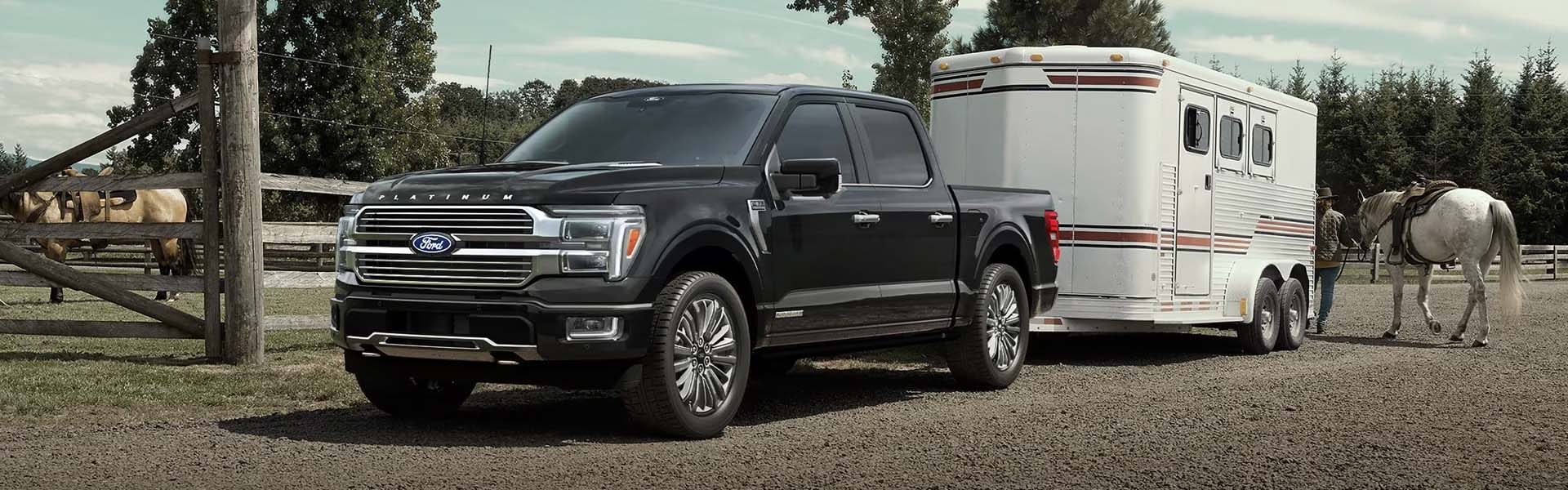 Un pickup Ford F-150 estacionado en una granja de caballos, un hombre transporta un caballo hacia un remolque ligero enganchado al vehículo.