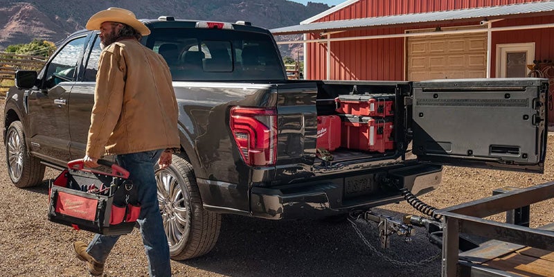 Un hombre que lleva una bolsa de herramientas camina junto a una Ford F-150.